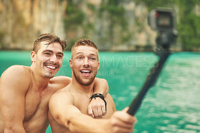 Buy stock photo Cropped shot of two young guys taking a selfie while out for a swim