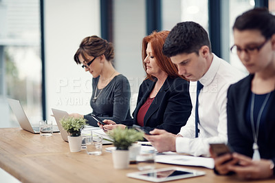 Buy stock photo Cropped shot of a group of businesspeople texting on their cellphones in an office