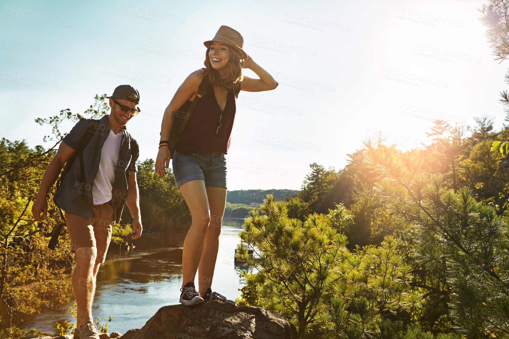 Buy stock photo Nature, hiking and couple walking on cliff at lake on adventure holiday in mountain with trees, sun, and water. Trekking, man and woman on travel vacation together at river, park or outdoor climbing