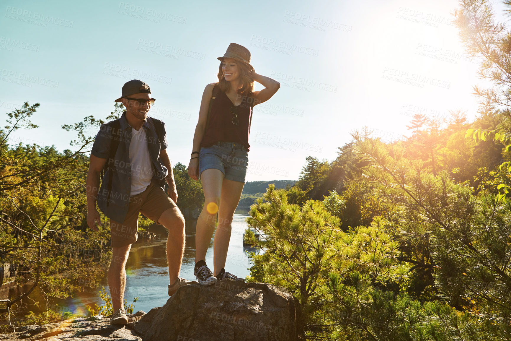 Buy stock photo Nature, hiking and couple walking on cliff at water on adventure holiday in mountain with trees, sun, and lake. Trekking, man and woman on travel vacation together at river, park or outdoor climbing