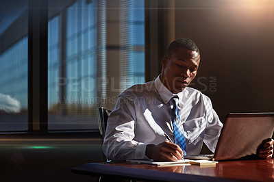 Buy stock photo Shot of a businessman taking notes while using his laptop