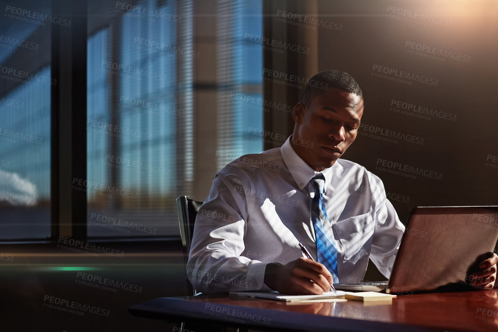 Buy stock photo Shot of a businessman taking notes while using his laptop