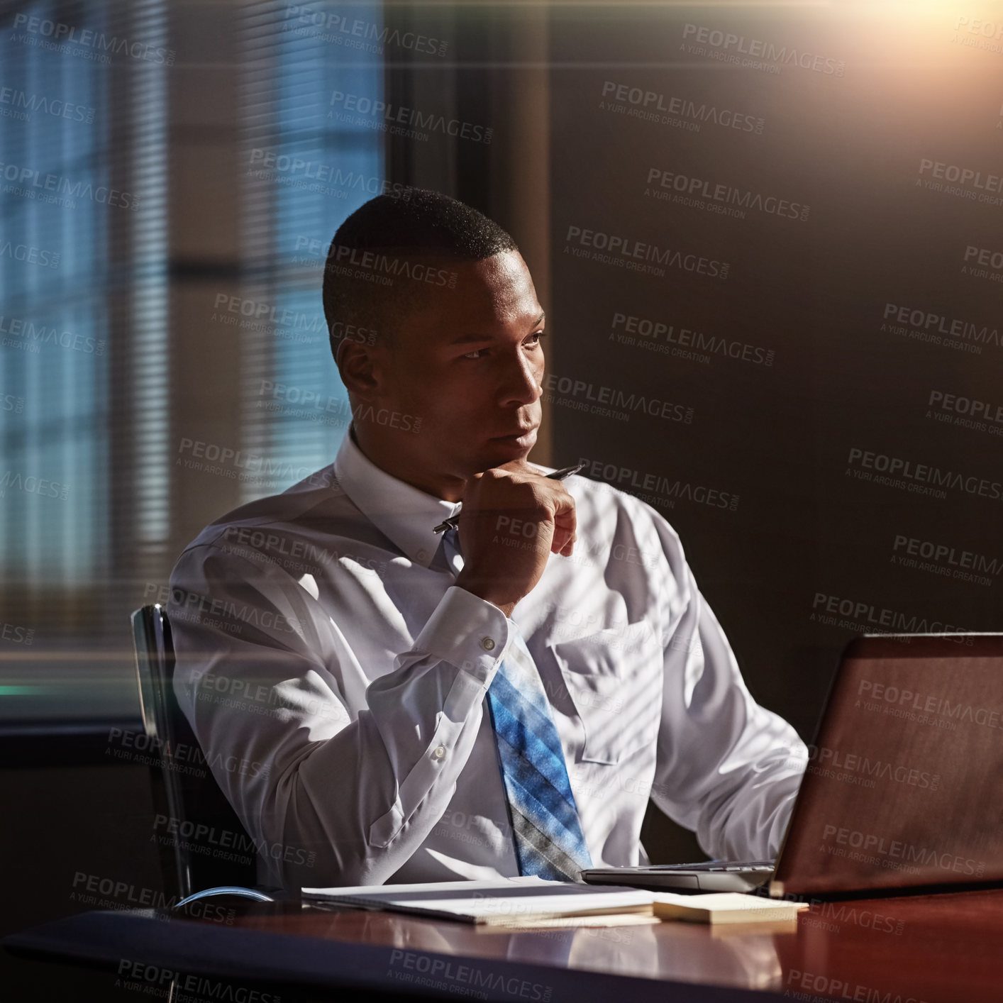 Buy stock photo Shot of a young man contemplating while using his laptop