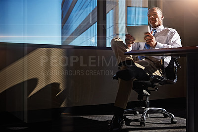 Buy stock photo Shot of a businessman using his digital tablet at his desk
