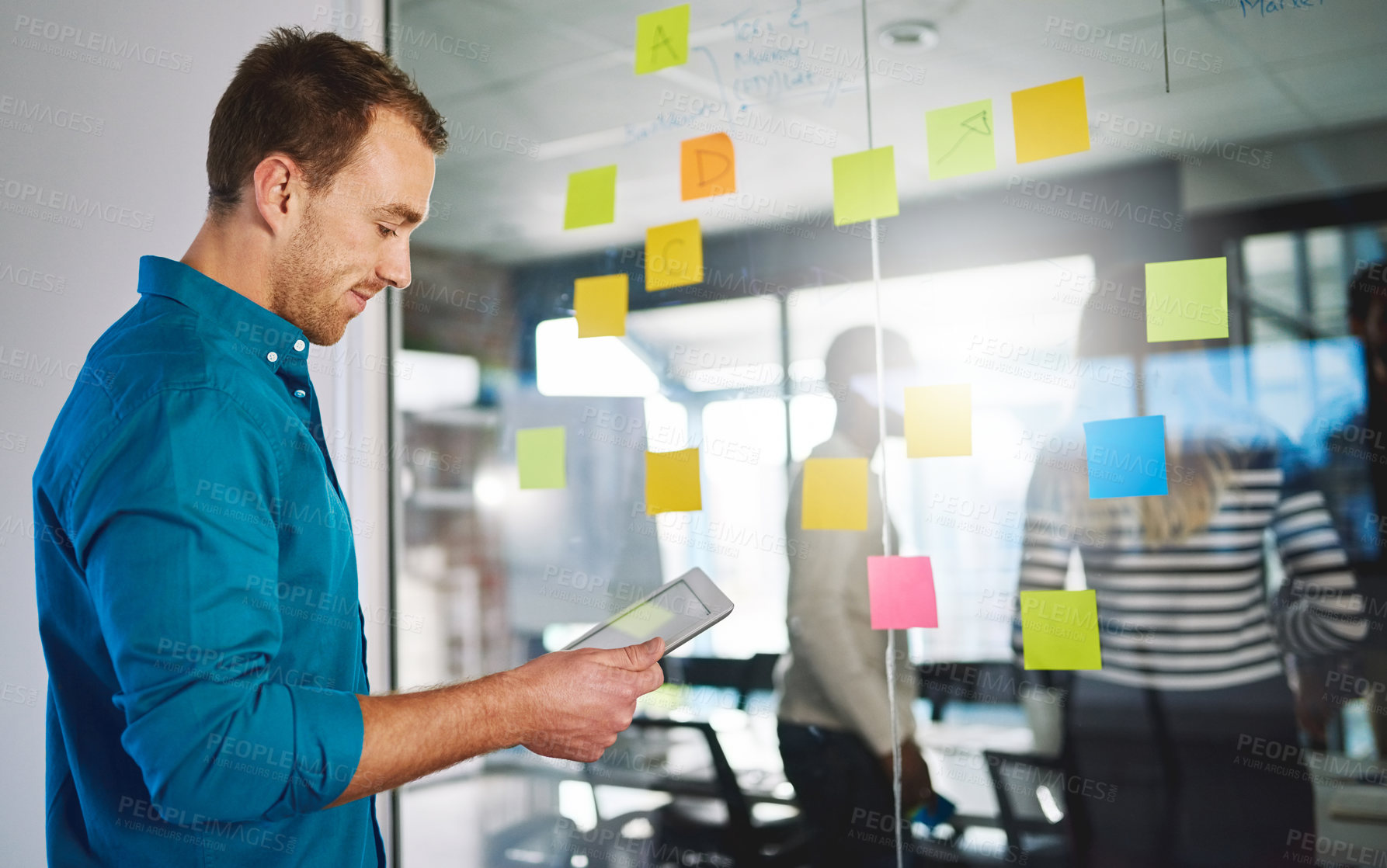 Buy stock photo Shot of a young man using a digital tablet during a brainstorming session at work