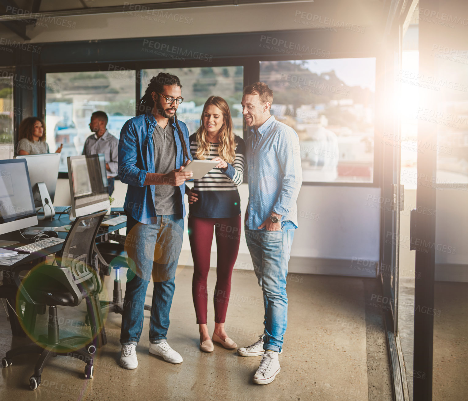 Buy stock photo Shot of three young designers talking over a digital tablet in their office