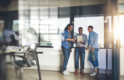 Buy stock photo Shot of three young designers talking over a digital tablet in their office