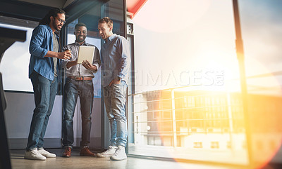 Buy stock photo Shot of three young designers talking over a digital tablet in their office