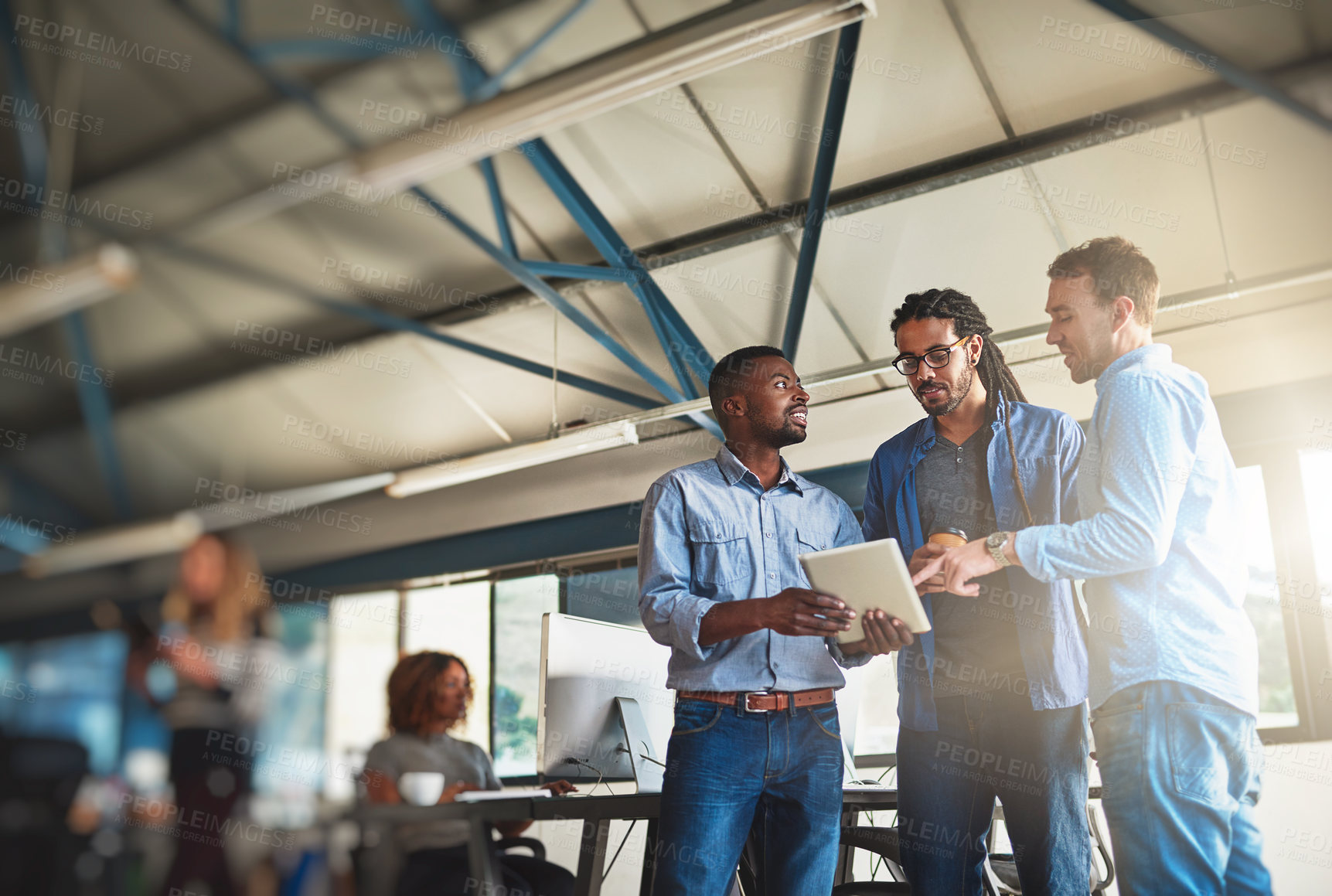 Buy stock photo Shot of three young designers talking over a digital tablet in their office