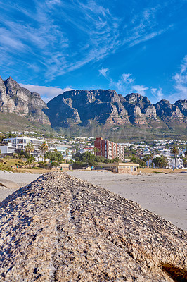 Buy stock photo Landscape, rock and beach with buildings, city and sky with mountain view, outdoor and summer in nature. Stone, boulder and environment with sand, hill and urban expansion on horizon in South Africa