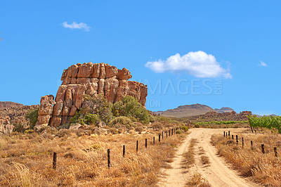 Buy stock photo Landscape, road and sky with rock, formation and geology at location, bush and clouds in summer. Countryside, stone and grave path at nature park, field and mountains with outcrop in South Africa