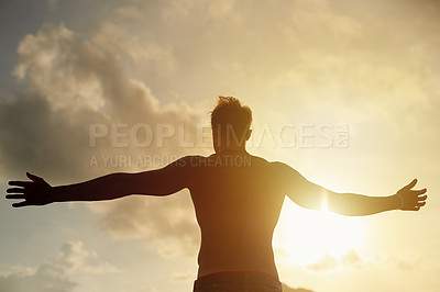 Buy stock photo Rearview shot of a young man with open arms silhouetted against a sunset