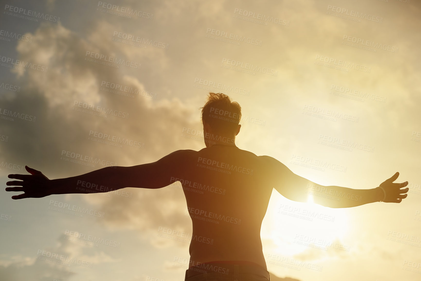 Buy stock photo Rearview shot of a young man with open arms silhouetted against a sunset