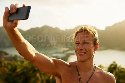 Buy stock photo Shot of a happy young man taking a selfie with his cellphone while on holiday