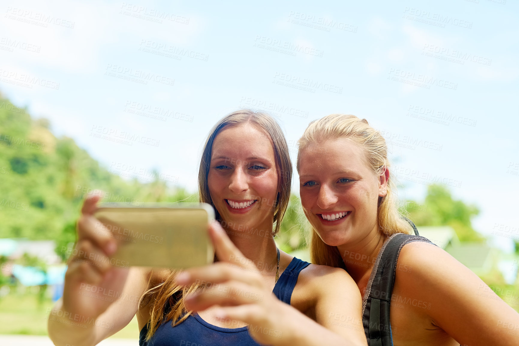Buy stock photo Cropped shot of two young girlfriends taking selfies on the beach