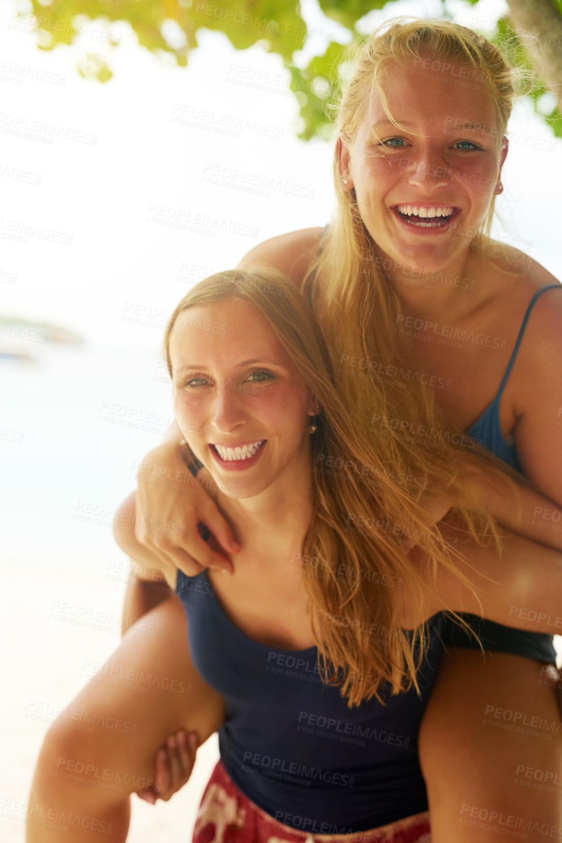 Buy stock photo Portrait of an attractive young woman piggybacking her friend on the beach