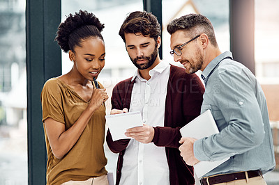 Buy stock photo Cropped shot of three businesspeople looking at a digital tablet in their office