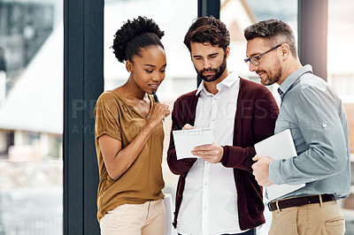 Buy stock photo Cropped shot of three businesspeople looking at a digital tablet in their office