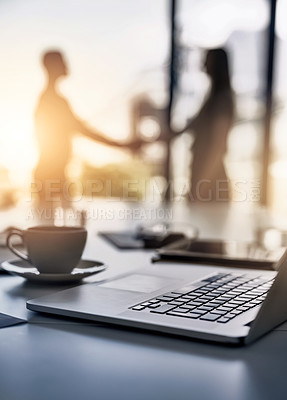 Buy stock photo Closeup shot of a laptop on a desk with businesspeople shaking hands in the background