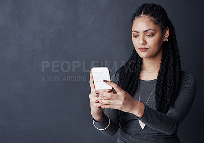 Buy stock photo Studio shot of a young woman using her cellphone against a grey background