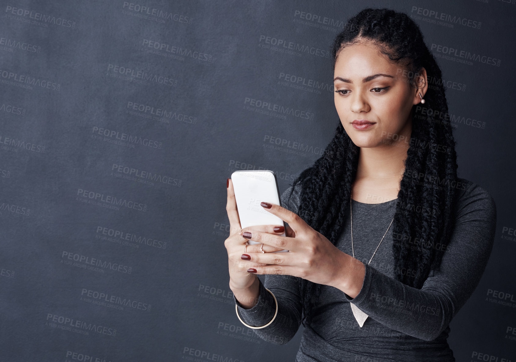 Buy stock photo Studio shot of a young woman using her cellphone against a grey background