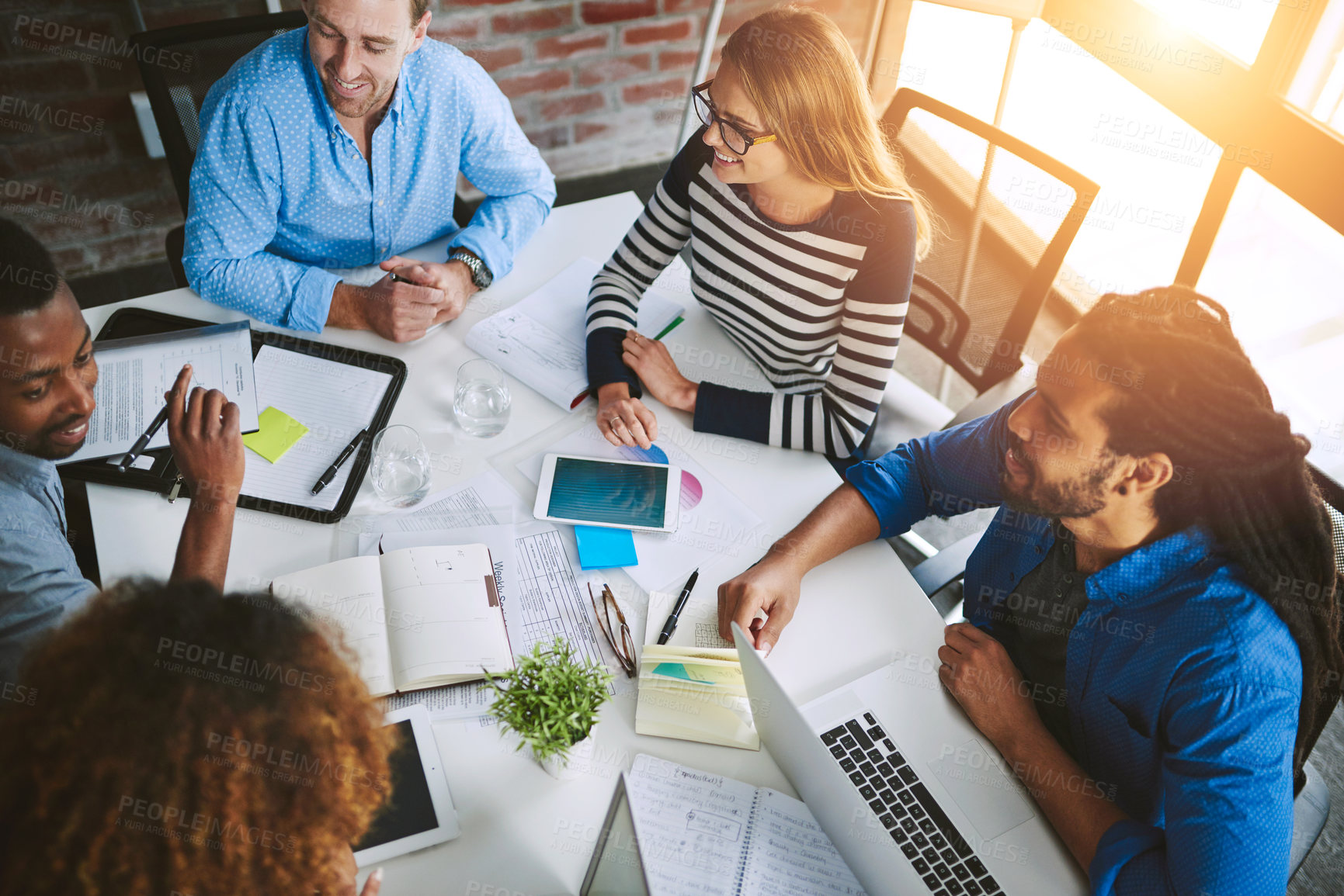 Buy stock photo Meeting, laptop and business people with notebook at table for teamwork, idea or planning. Above, diversity and staff with tech for documents, discussion or deadline at printing firm with lens flare