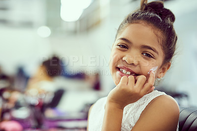 Buy stock photo Portrait of a cute little girl applying moisturizer to her face while sitting in a dressing room