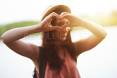 Buy stock photo Portrait of a happy young woman making a heart shape with her hands while exploring outdoors