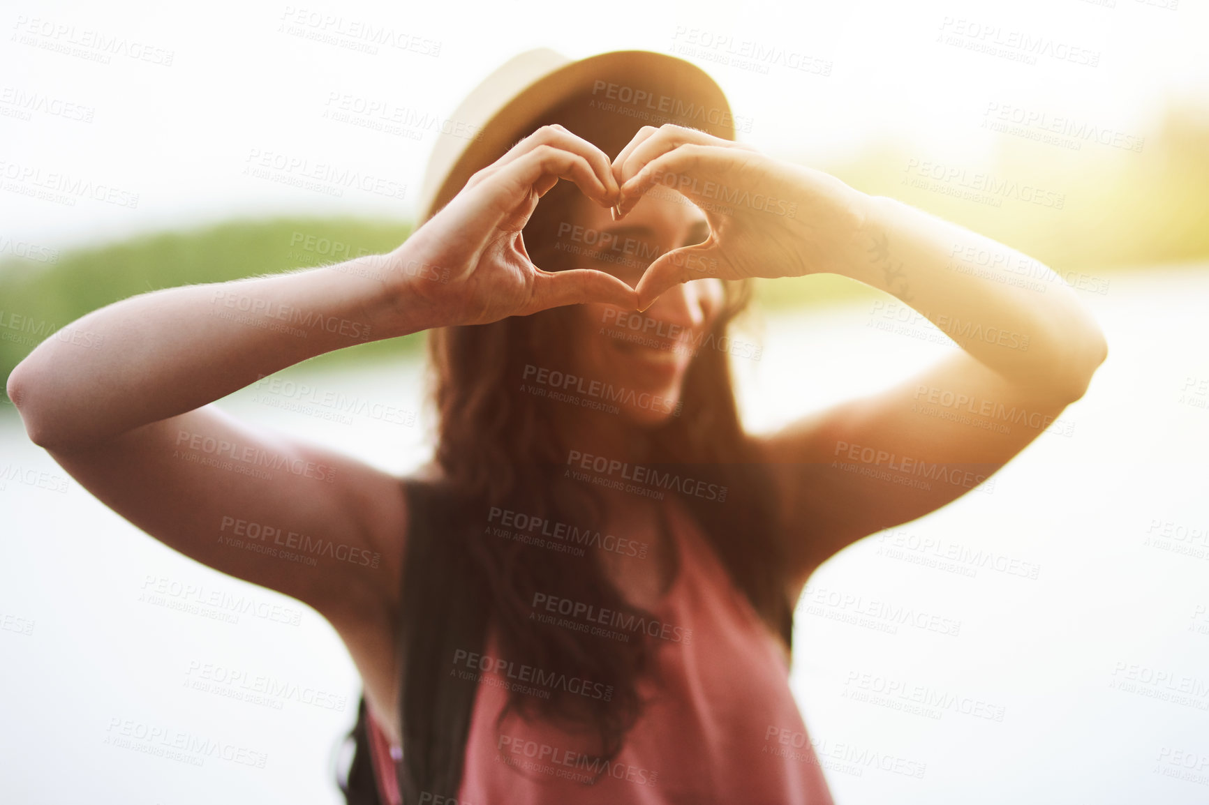 Buy stock photo Portrait of a happy young woman making a heart shape with her hands while exploring outdoors