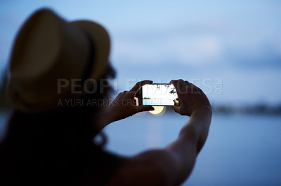 Buy stock photo Rearview shot of an unidentifiable young woman photographing a dusky landscape with her phone