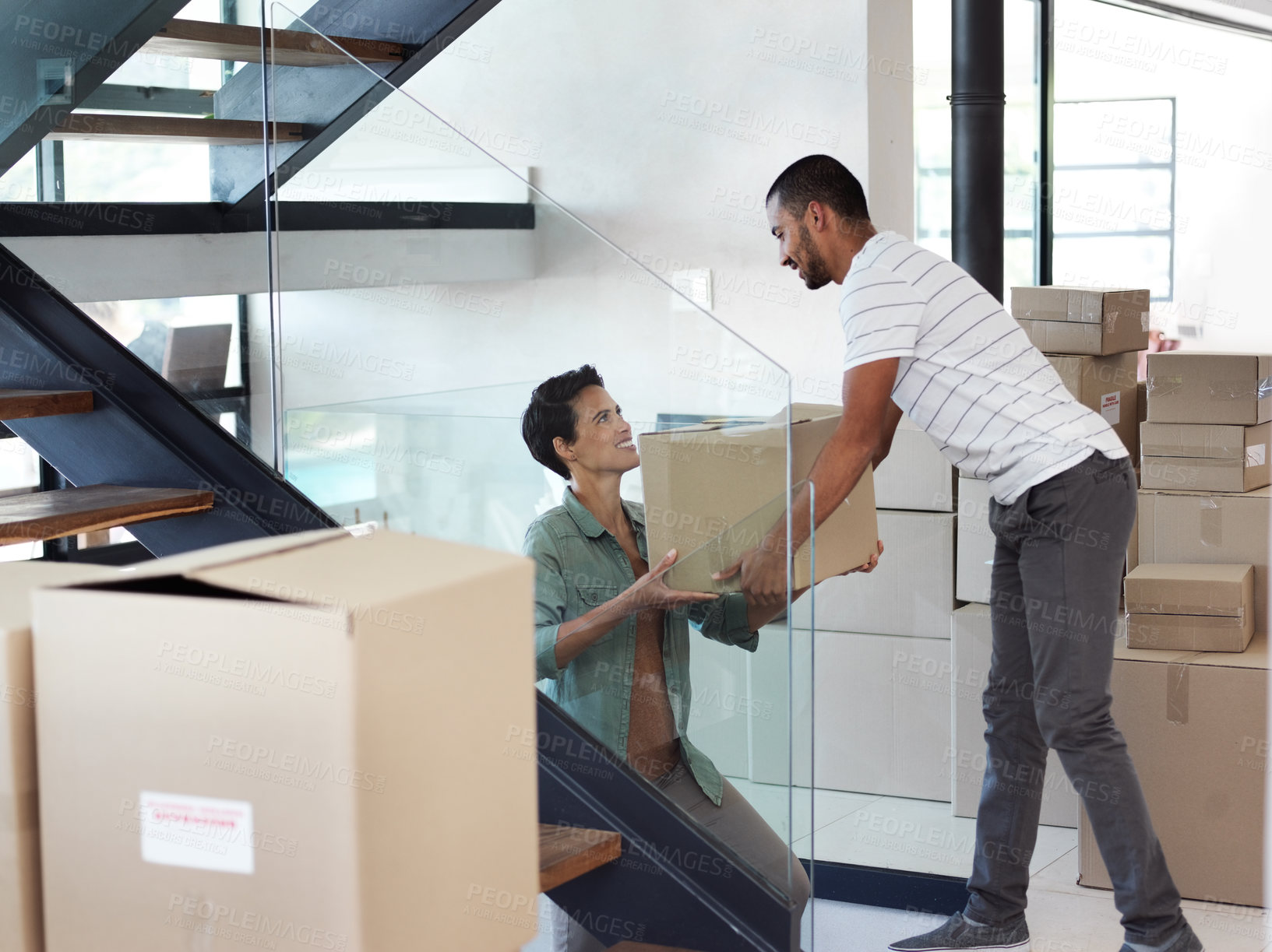 Buy stock photo Shot of a happy young couple passing boxes to each other while moving into their new home