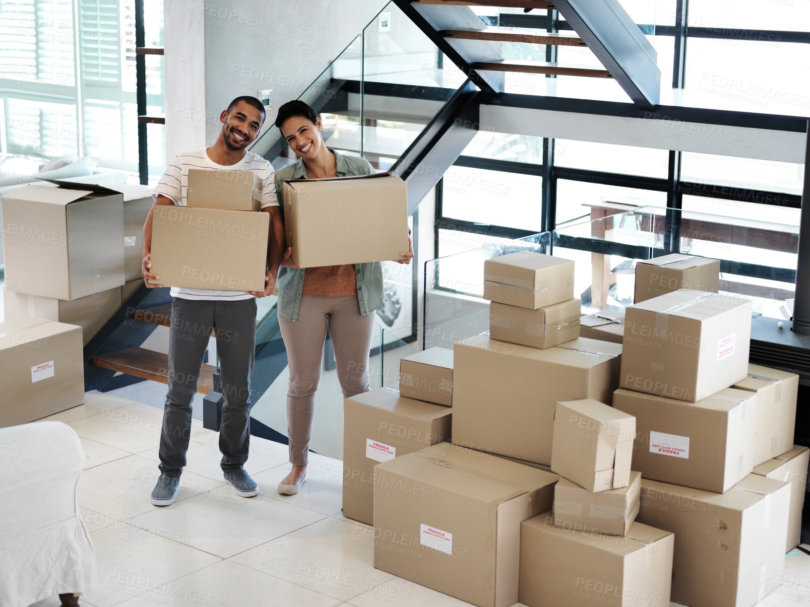 Buy stock photo Portrait of a happy young couple carrying boxes while moving into their new home