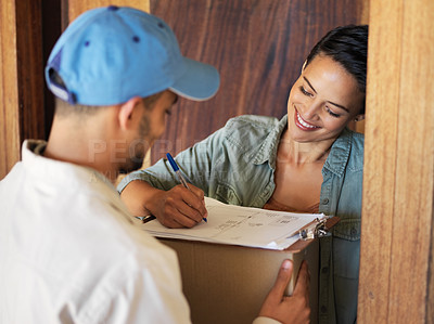 Buy stock photo Shot of a young woman standing at her front door signing for a package from a courier
