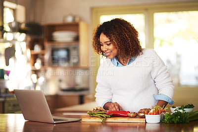 Buy stock photo Shot of a young woman using a laptop while preparing a healthy meal at home