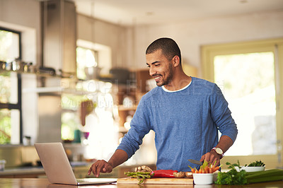 Buy stock photo Shot of a happy young man using a laptop while preparing a healthy meal at home