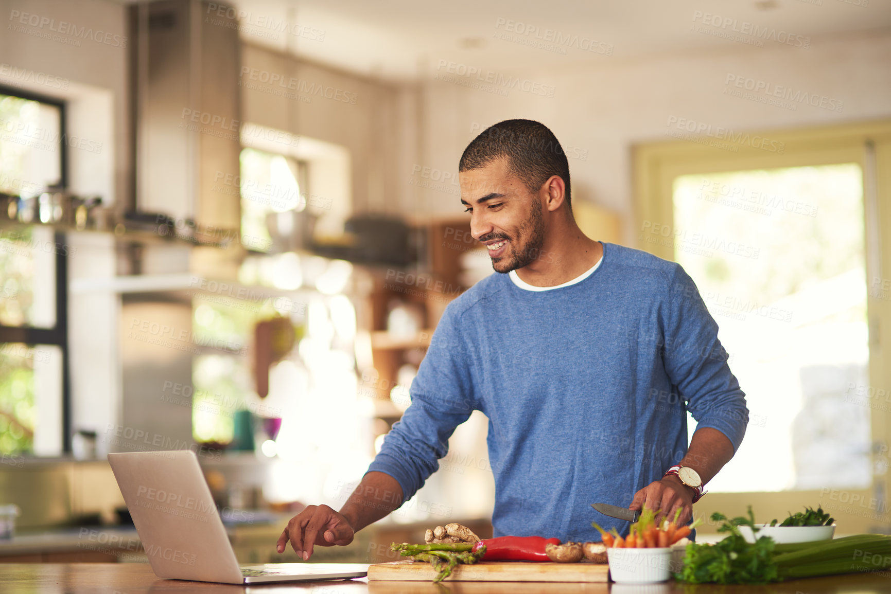 Buy stock photo Shot of a happy young man using a laptop while preparing a healthy meal at home