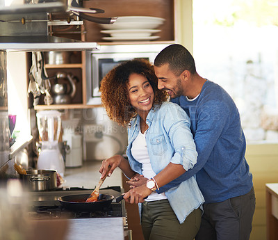 Buy stock photo Shot of a young man hugging his wife while she prepares a meal at home