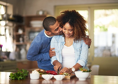 Buy stock photo Shot of a young man kissing his wife while she prepares a healthy meal at home