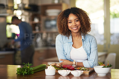 Buy stock photo Portrait of a happy young woman preparing a healthy meal at home with her husband in the background