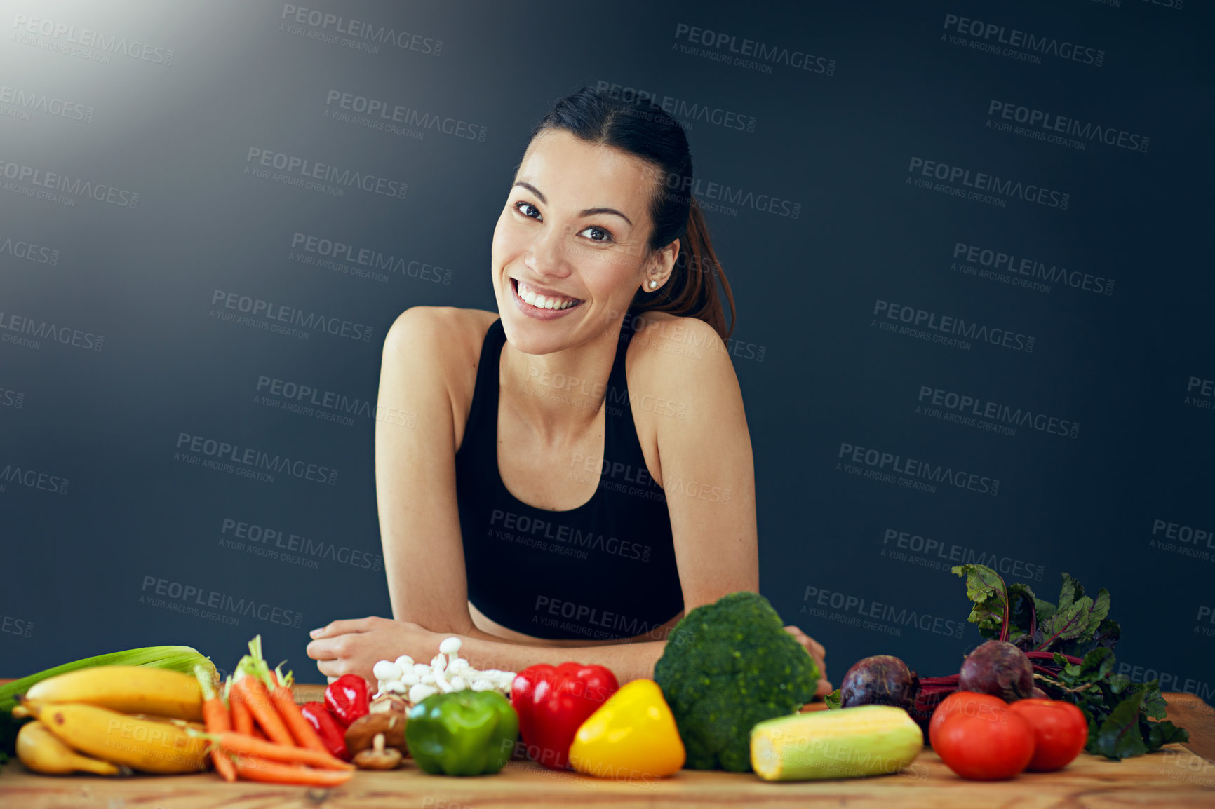 Buy stock photo Studio portrait of an attractive young woman posing with a variety of vegetables on the table