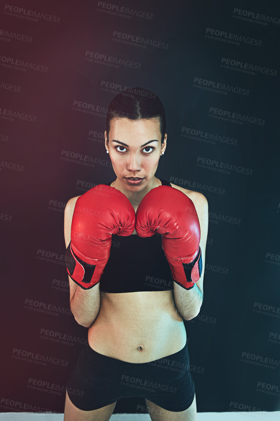 Buy stock photo Shot of a young woman wearing boxing gloves against a dark background