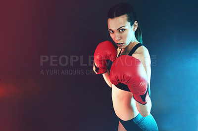Buy stock photo Shot of a young woman wearing boxing gloves against a dark background