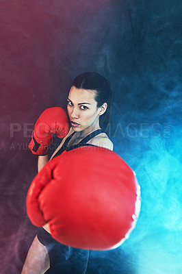 Buy stock photo Shot of a young woman wearing boxing gloves against a dark background