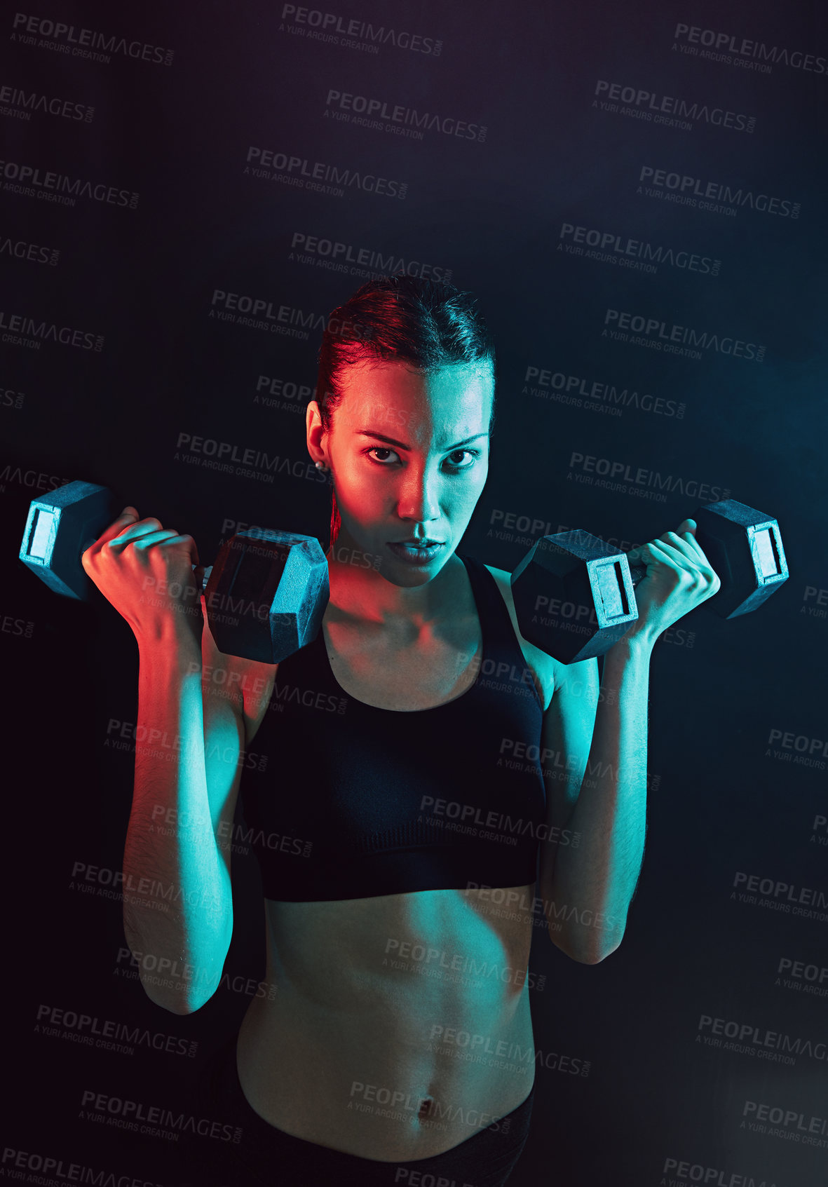 Buy stock photo Shot of a young woman lifting weights against a dark background