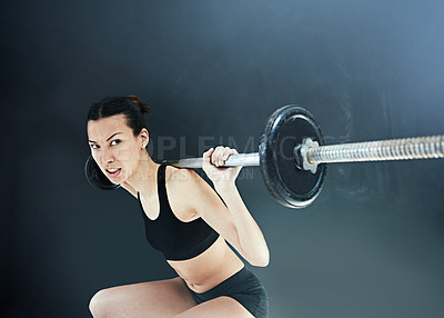 Buy stock photo Shot of a young woman lifting weights against a dark background