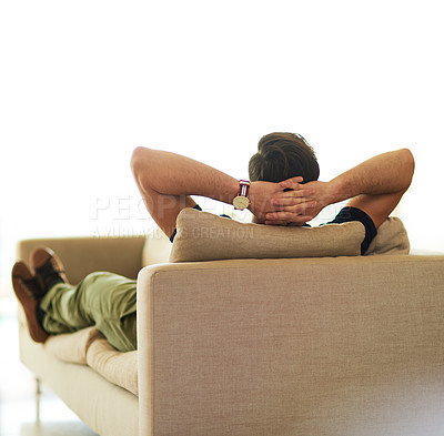 Buy stock photo Rearview shot of an unrecognizable young man relaxing on his sofa at home