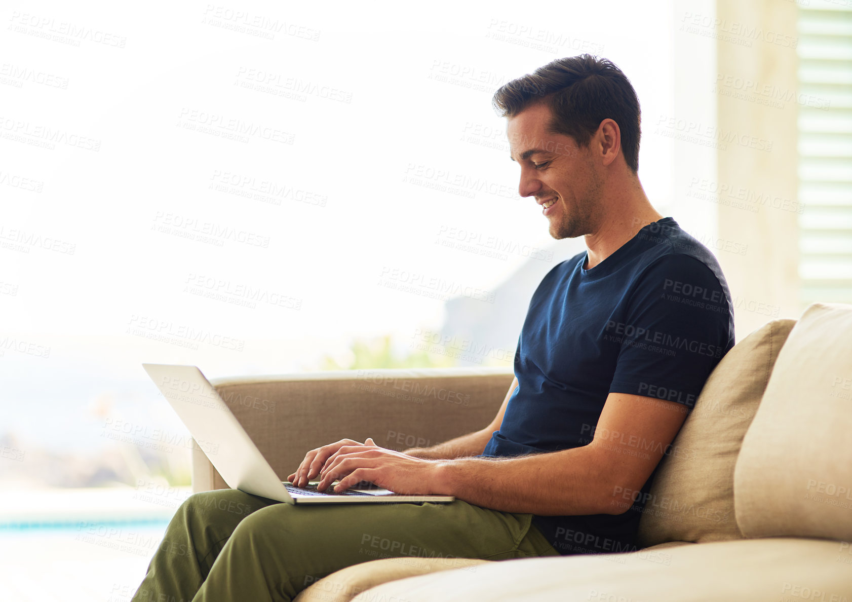 Buy stock photo Shot of a handsome young man using his laptop while sitting on the sofa at home