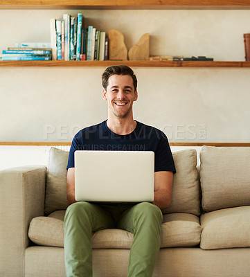 Buy stock photo Portrait of a handsome young man using his laptop while sitting on the sofa at home