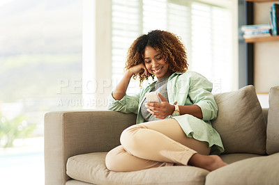 Buy stock photo An attractive young woman using her cellphone while relaxing on the sofa at home