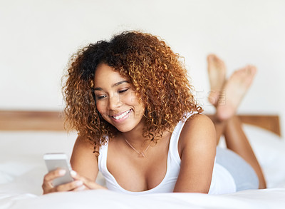 Buy stock photo Shot of a young woman texting while lying on her bed